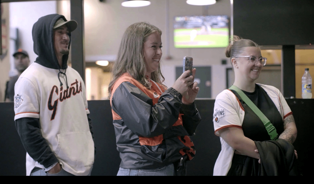 A group of San Francisco Giants fans taking video of someone in the HitTrax Suite